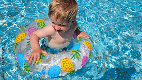 Sweet, blond boy swimming with a pineapple swim ring. Summer pool time. Childhood memories. High quality photo