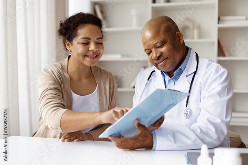 Happy African American doctor reviewing medical records with smiling black millennial female patient during visit in modern clinic, therapist man discussing test results with woman, closeup