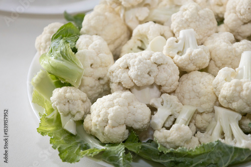 Fresh and raw cauliflower on the white plate.  The cauliflower  -  vegetable is cut into pieces on white background. The vegetable is divided into inflorescences on the plate