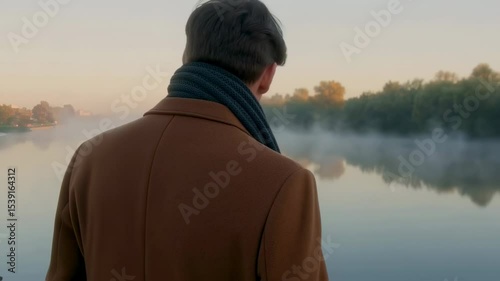 Slow motion portrait of a man standing by a foggy lake at dawn.  
