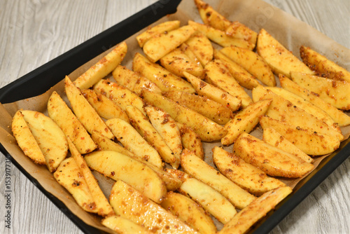 Country-style potatoes - wedges with skins in spices on a baking sheet. Raw