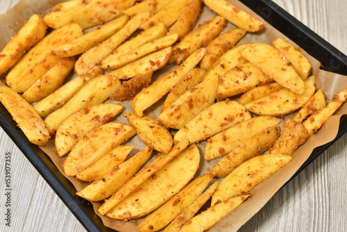 Country-style potatoes - wedges with skins in spices on a baking sheet. Raw
