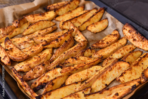 baked Country-style potatoes - wedges with skins in spices on baking sheet.