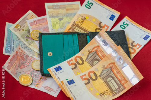 Wallet with euro and Bulgarian lev banknotes and coins on red background. Bulgaria, transition to Euro, finance and budgeting. Concept of personal money, savings, financial international spending