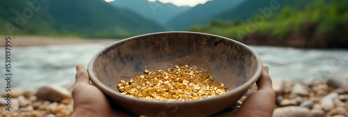 A bowl filled with golden nuggets is held up against a scenic river and mountain backdrop, symbolizing wealth found in nature's embrace.
