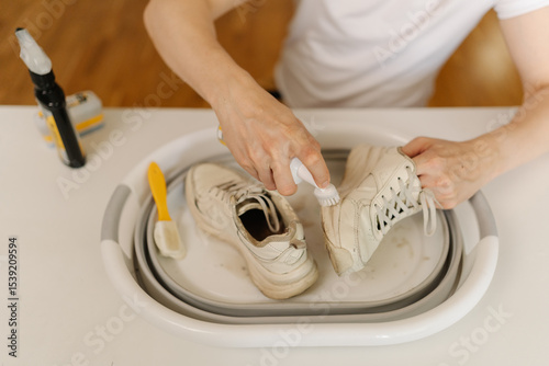 Photography Process of cleaning white dirty sneakers with scrubbing brush and detergent, removing stubborn stains from footwear in white basin, preserving shoe hygiene and appearance thorough washing work