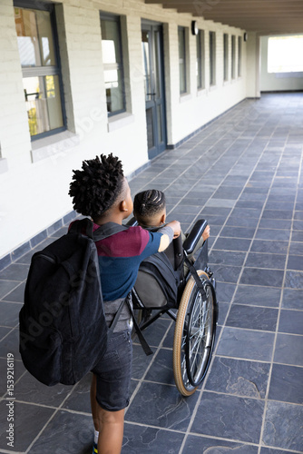 Walking together in school hallway, diverse boys showing friendship, one pushing wheelchair