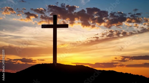 Silhouette of a cross atop a hill under a dramatic sunset sky with orange and gold clouds visible in the background.