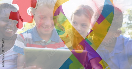 Sharing digital tablet, group of children sitting on grass in park, wearing bright summer clothing