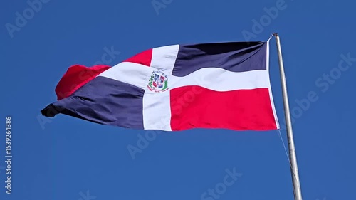 Dominican Republic flag waving majestically in the wind against a clear blue sky, vibrant national colors fluttering powerfully with strong gusts, patriotic and symbolic scene in daylight