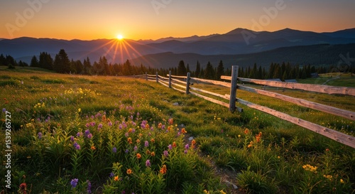 Peaceful sunset over a mountain landscape, with wildflowers in a grassy meadow and a rustic wooden fence in the foreground.