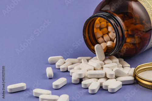 White tablets spilling from a brown bottle on colored surface