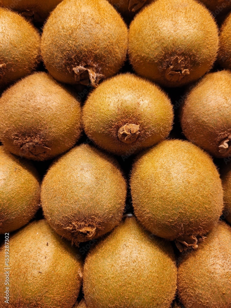Fototapeta premium Stacked kiwis forming a fresh and vibrant background. The image highlights the natural texture and earthy tones of the fruit, ideal for healthy food concepts, packaging design, or organic lifestyle.
