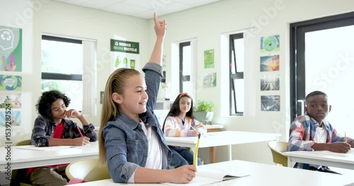 Multiracial students in classroom smiling and writing in notebooks during school lesson