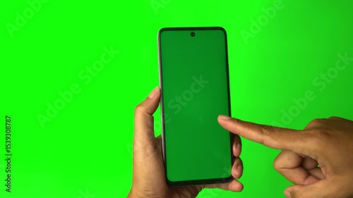 Hand holding smartphone with chroma green screen, finger pointing at screen. Green background