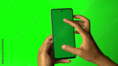 Hand holding smartphone with chroma green screen, fingers pinch to zoom. Green background