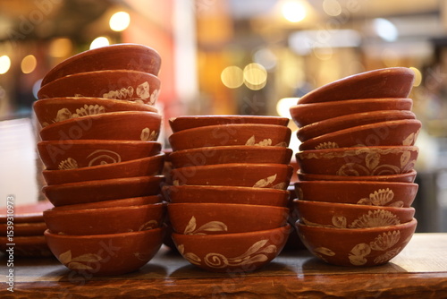 Beleza rústica em pilhas: tigelas de barro artesanais, com seus desenhos únicos, empilhadas em uma feira. A imagem celebra a textura da cerâmica e a riqueza do trabalho manual.