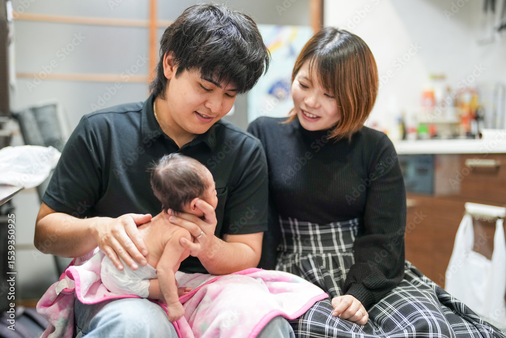 Obraz premium A two-week-old Japanese baby lies wrapped in a pink blanket, held close in the arms of loving parents in their early twenties, quietly drinking milk from a baby bottle in a warm, peaceful moment.