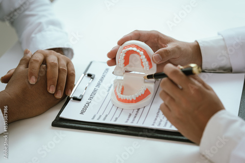 Bild auf Leinwand A dentist uses a pen to explain a dental model to a patient, discussing oral health and treatment options
