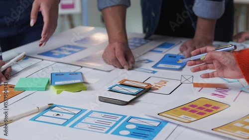 Software engineers collaborating on mobile application design, developing user interface and user experience through paper prototyping with smartphone at creative workspace
