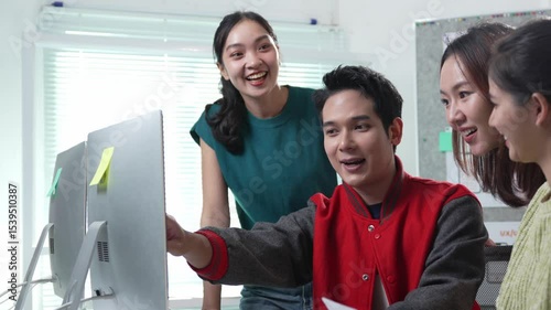 Young Asian designers team discussing new project together in modern office, pointing at computer screen, sharing ideas, collaborating on user interface design