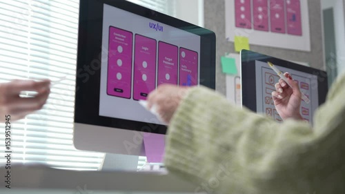 User experience and interface designers collaborating on mobile app login screen design, analyzing wireframes and user flow on desktop computer with printed drafts in modern office workspace