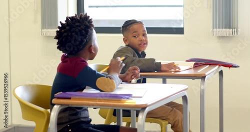 In school, two multiracial boys collaborating on homework at classroom desk, sharing ideas