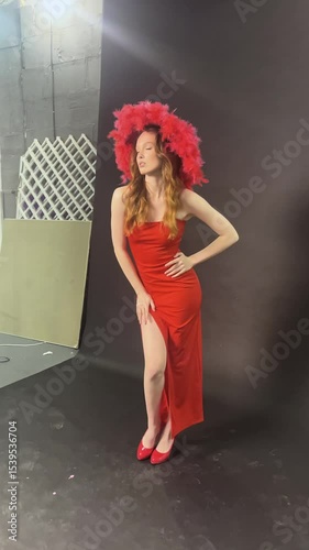 Woman poses elegantly in red dress and vibrant hat during studio shoot