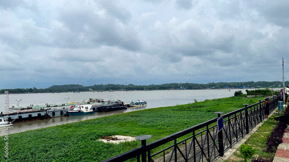 Fototapeta premium Cloudy Sky Over a Riverside Dock with Boats in a Peaceful Countryside Setting.