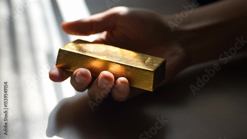 Holding gold bar in hand with natural light - person inspects precious metal before investing
