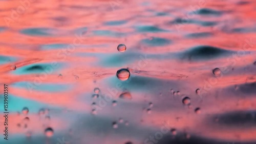 Serene Water Surface Reflects Soft Hues Of Pink And Blue Showcasing Ripples And Suspended Droplets