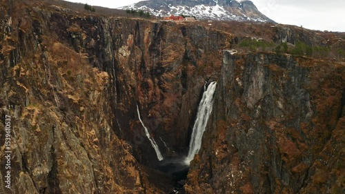 Voringsfossen waterfall with powerful stream cascading down deep gorge framed by imposing barren cliffs. Distant mountain under sky in Norway
