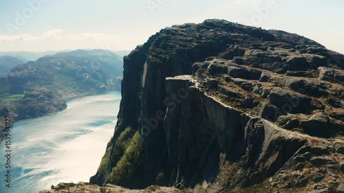 Pulpit Rock presents iconic flat top extending over expansive Lysefjord in Norway. Grandeur of landscape with distant mountains under clear sky
