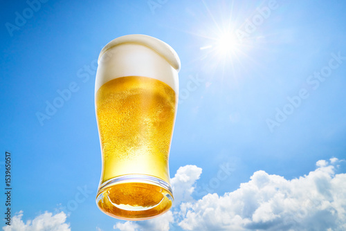 冷えたビールの泡がグラスからこぼれ落ちる、夏の青空に太陽の光の背景