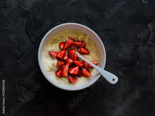 Millet porridge with fresh strawberries in a bowl on a dark background, top view