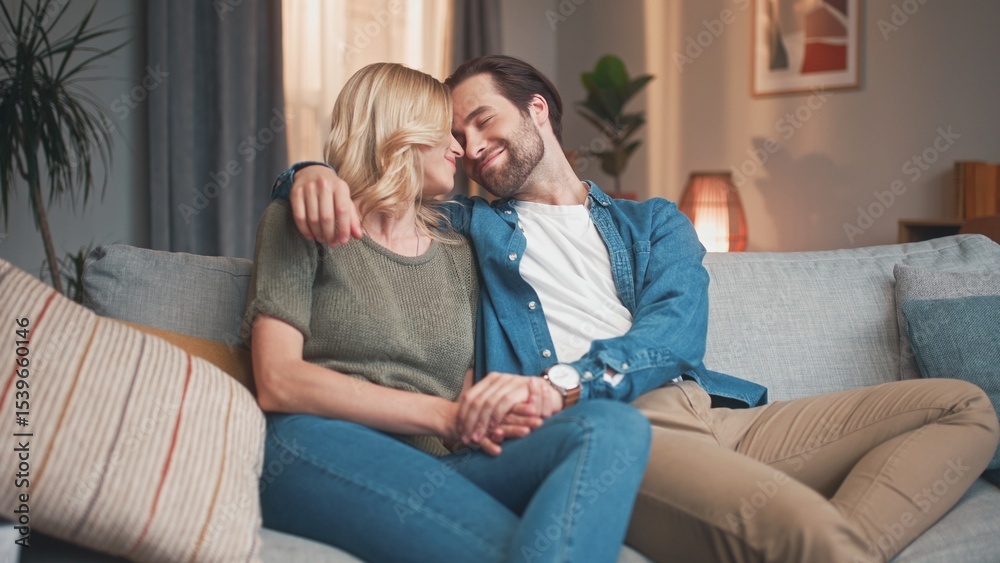 Cute husband and gorgeous wife sitting on sofa hugging and cuddling, kissing together. Lovely couple of beautiful man and woman having great time at home in living room. Love concept. Cute husband and gorgeous wife sitting on sofa hugging and cuddling, kissing together. Lovely couple of beautiful man and woman having great time at home in living room. Love concept.