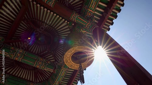 Illuminated Temple Bell Beneath Decorative Roof Against Clear Blue Sky on Bright Sunny Day