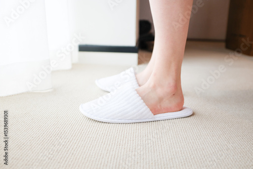 Feet wearing hotel slippers standing in front of glowing hotel window