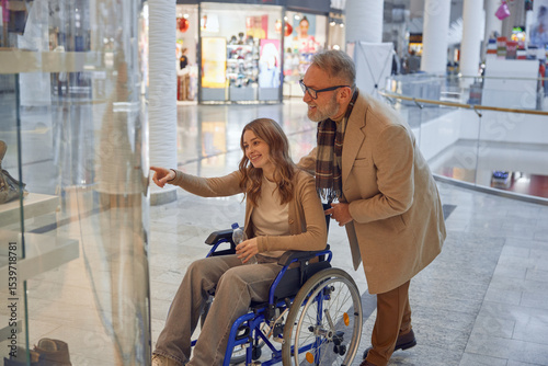 Family moment at shopping mall, mature granddad helping his granddaughter in a wheelchair