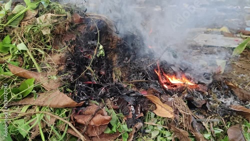 A small fire ignites dry leaves and branches, producing smoke outdoors. 