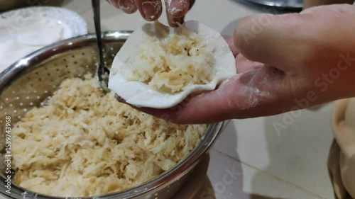 Close-up footage of hands making dumplings, placing freshly prepared fillings into the dough in the kitchen, showcasing traditional cooking techniques and fresh ingredients.