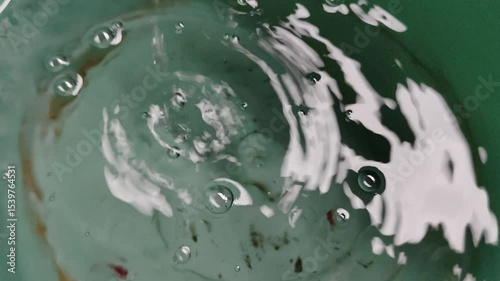 The scene of the interaction of ripples and bubbles in the green water bucket, which displays fluid dynamics and calm serenity.