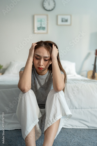 Depressed Asian woman feel upset while sitting alone on floor in bedroom.