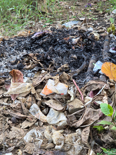 Close-up of outdoor burning pile with glowing embers and dry leaves in open field surrounded by scattered trash