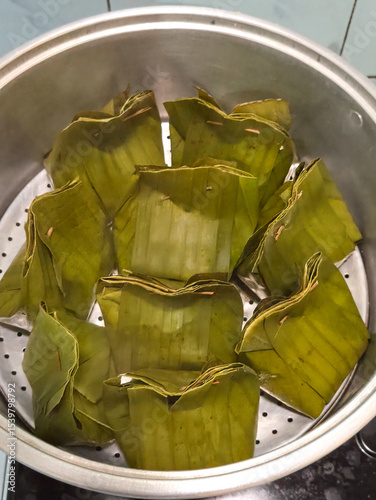 Fresh banana leaf parcels stacked tightly in boiling pot during traditional Indonesian or Southeast Asian cooking