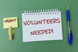 Volunteers Needed Campaign Banner written on the notebook on a green background