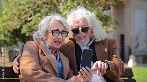 A delightful elderly couple happily sharing a smartphone experience, engrossed in laughter and conversation as they explore applications, highlighting their joyful bond and enjoyment of technology