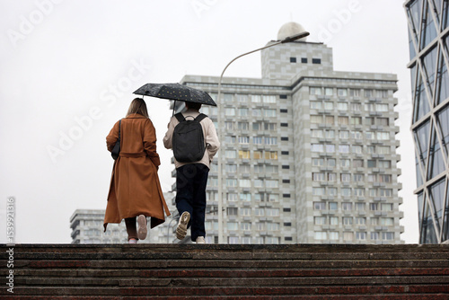 Couple with one umbrella climb the steps on a street. Rainy weather in summer city