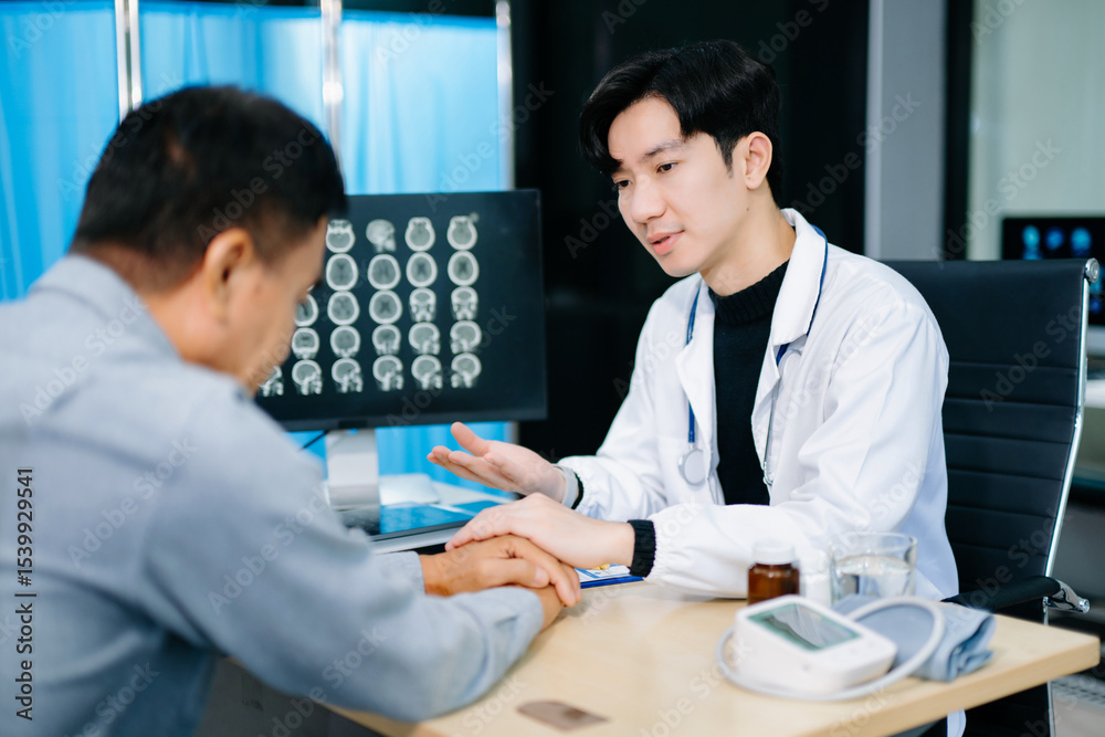 Fototapeta premium Young Asian doctor shows compassion and explains brain scan results to a patient in a clinic. Concept of medical support, neurology
