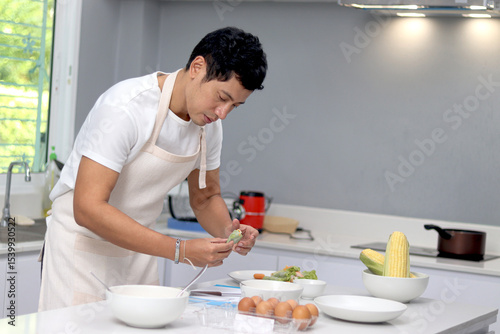 Asian man with apron preparing healthy breakfast meal in the kitchen. Happy man cooking food in kitchen at home.